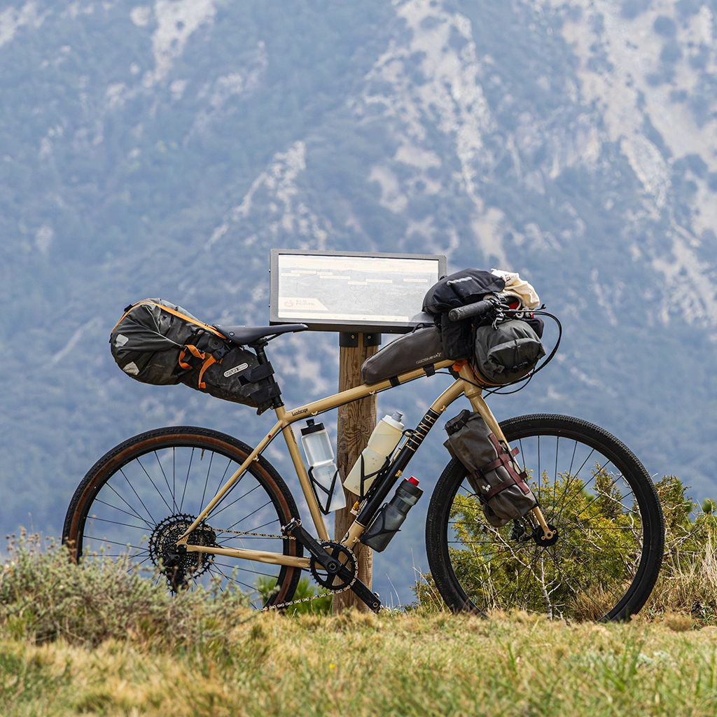 Bicicleta de gravel con alforjas apoyada en un post con montaña de fondo