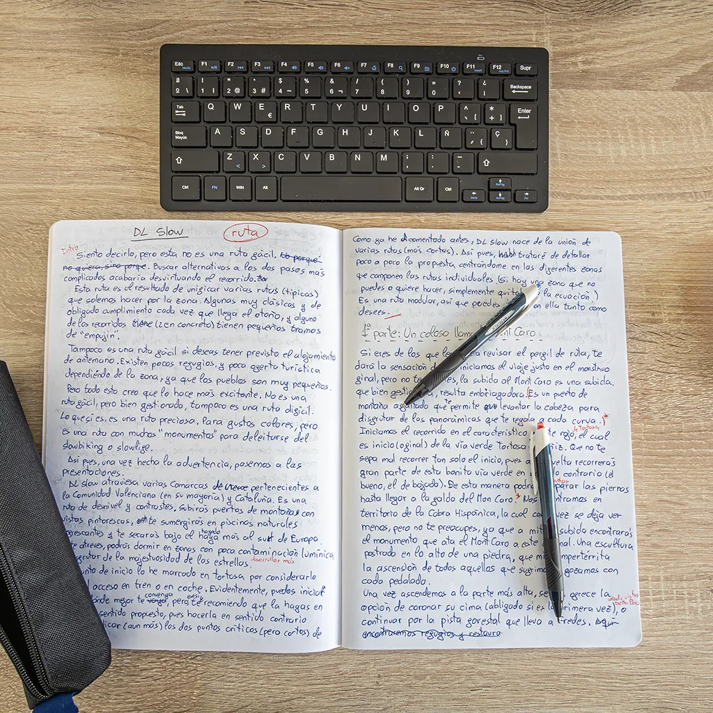 Libreta con un texto escrito a mano junto a dos bolígrafos y un estuche